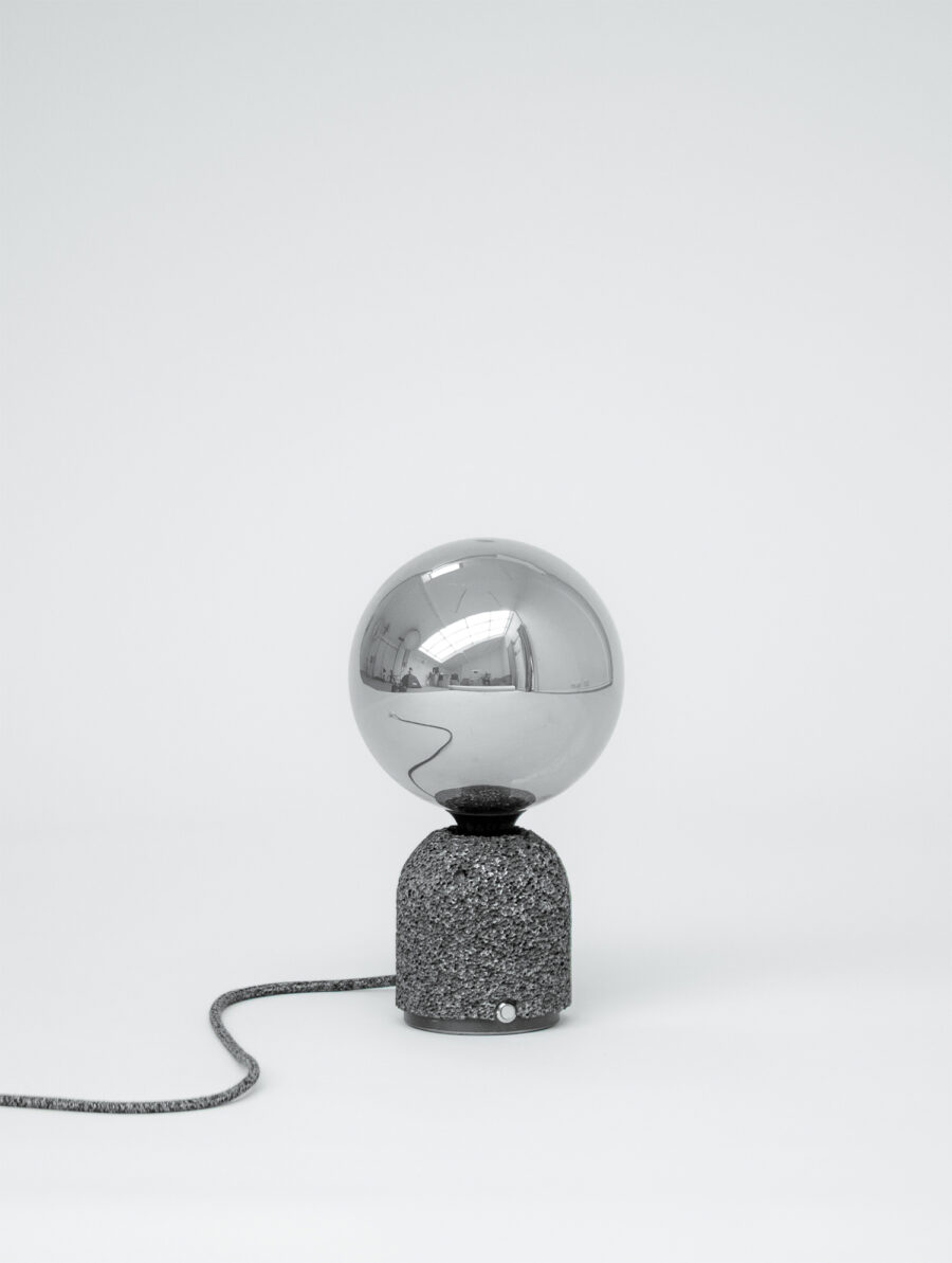 Modern table lamp with a dark aluminum foam base and a mirrored globe bulb, shown against a plain white background with its fabric-covered power cord extending outward.