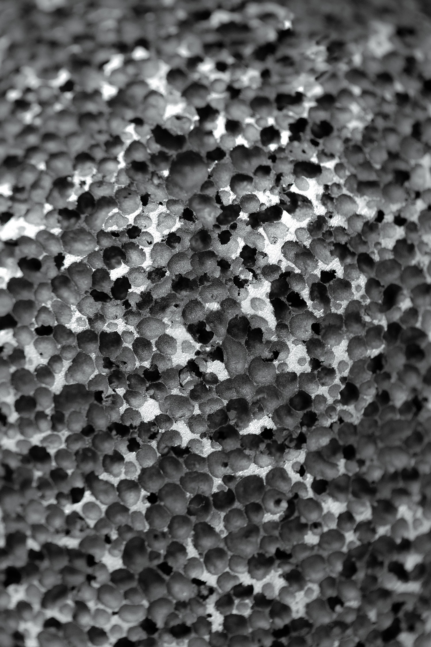 Close-up of a porous dark aluminum foam surface with irregular black and grey speckled texture