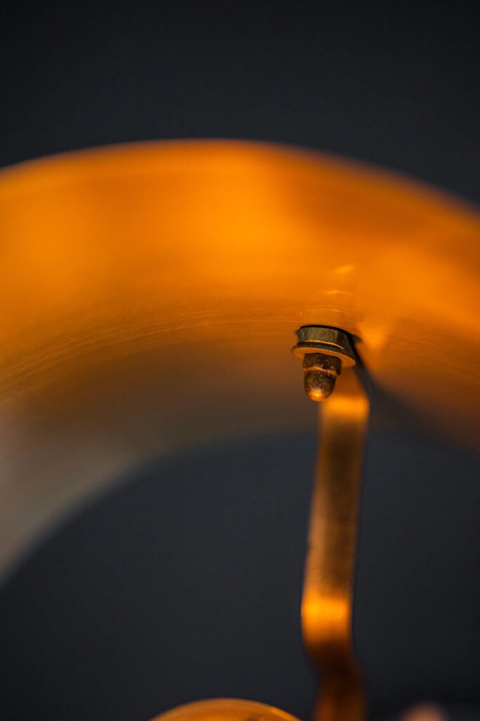Close-up view of the interior of a brass lampshade with a warm, golden hue. A bolt is attaches the shade to the frame, highlighted against a dark background.