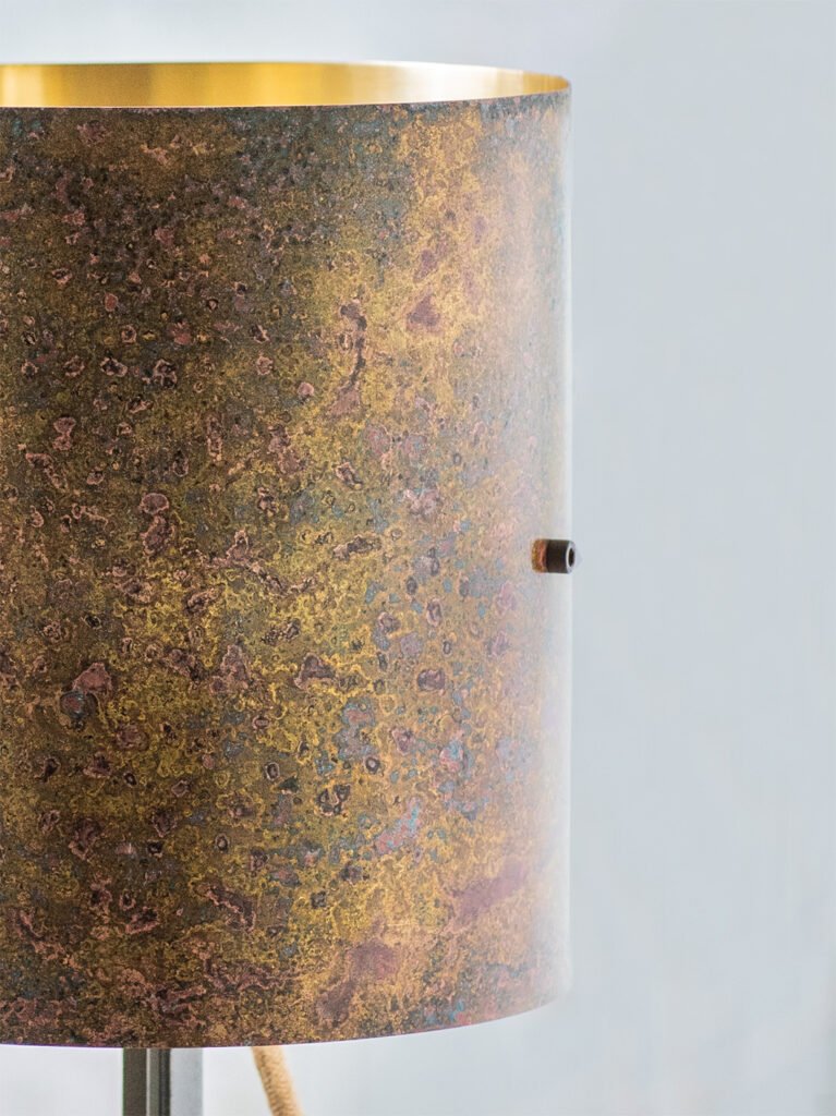 Close-up of a textured brass lampshade with a mottled surface featuring earthy tones of brown, yellow, and hints of purple. The edge of its reflective gold interior is faintly visible.