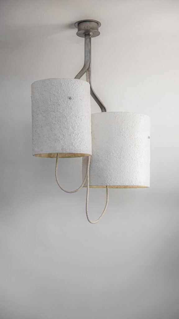 Steel chandelier with two stone-effect cylindrical shades on an elegantly twisting frame. Textile cables hang stylishly, mounted on a circular rose, standing out as a striking decor piece.