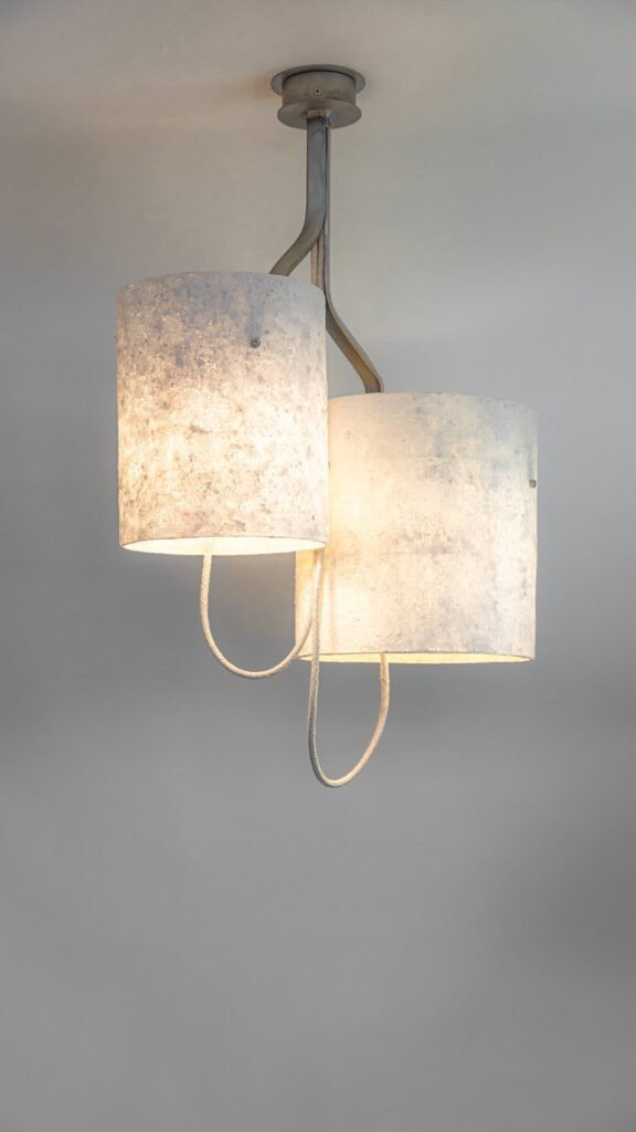 Modern steel chandelier with two stone-effect cylindrical shades on an elegantly twisting frame. Textile-covered cables enhance the design, while warm light creates a cozy, contemporary ambiance.