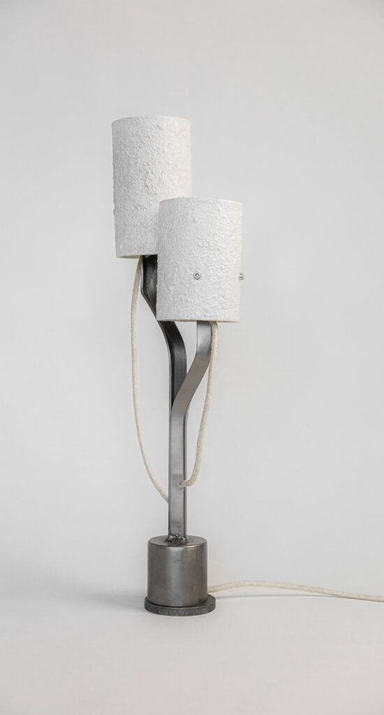 Modern lamp with stone-effect cylindrical shades on metallic arms branching from a steel base. Textile cord integrates seamlessly, blending practicality with a minimalist, contemporary design.