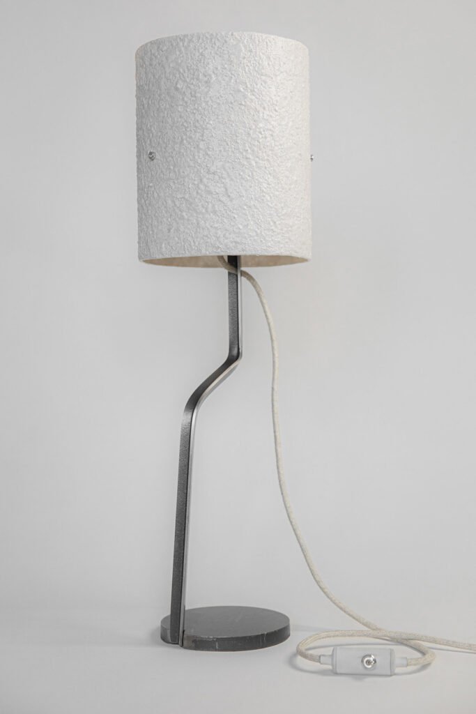 Modern table lamp with a white stone-effect shade. Curved steel stand connects to a circular base for stability, while a textile cord adds practicality to its minimalist, elegant design.