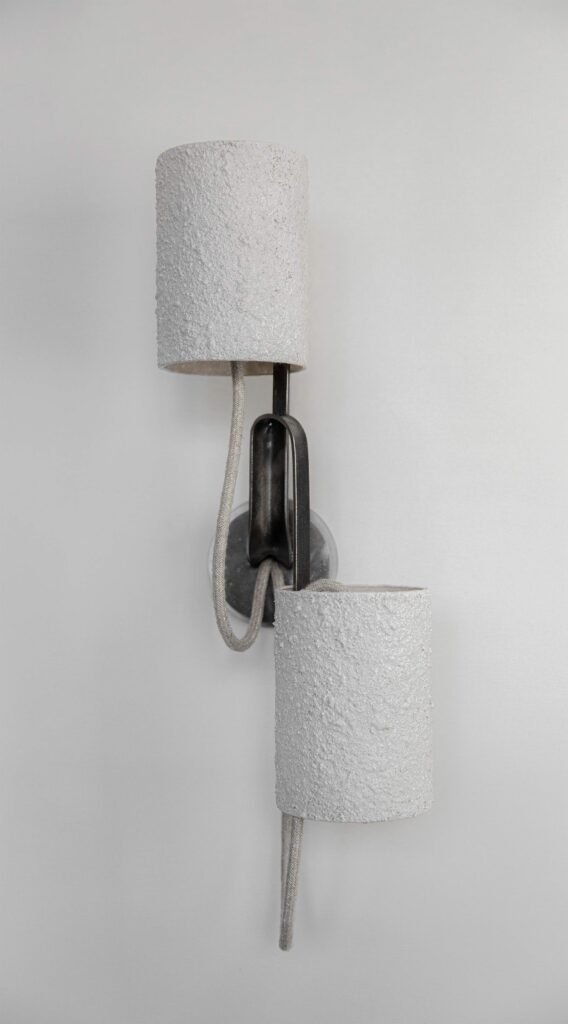 Wall-mounted light with two cream off-white stone-effect cylindrical shades on curved steel arms. Textile cords add industrial flair, while its clean lines highlight the modern aesthetic as decor.