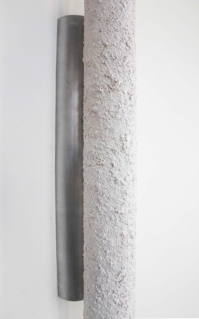 Close-up of a wall-mounted tube light fixture with an unlit textured stone-like surface. Intricate detailing contrasts with the sleek brushed steel rose, blending ruggedness with refined design.