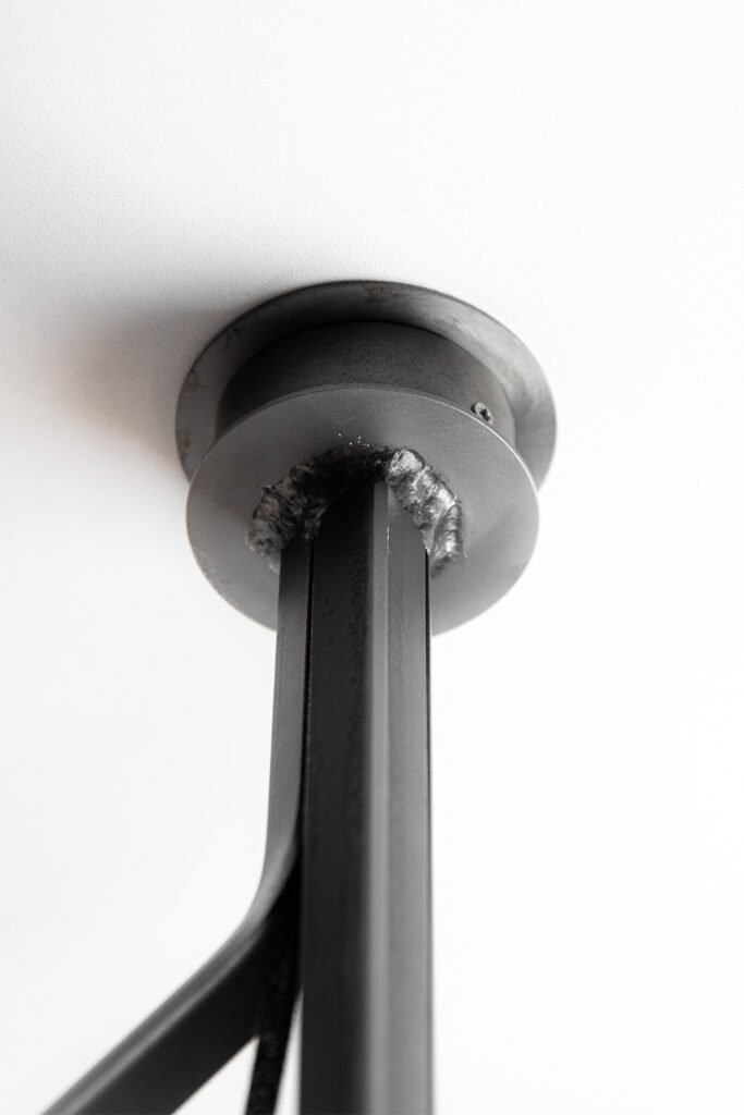 Close-up of a chandelier's circular steel ceiling rose with neatly attached textile cables. Partially visible curved steel frame highlights its seamless, elegant integration and craftsmanship.